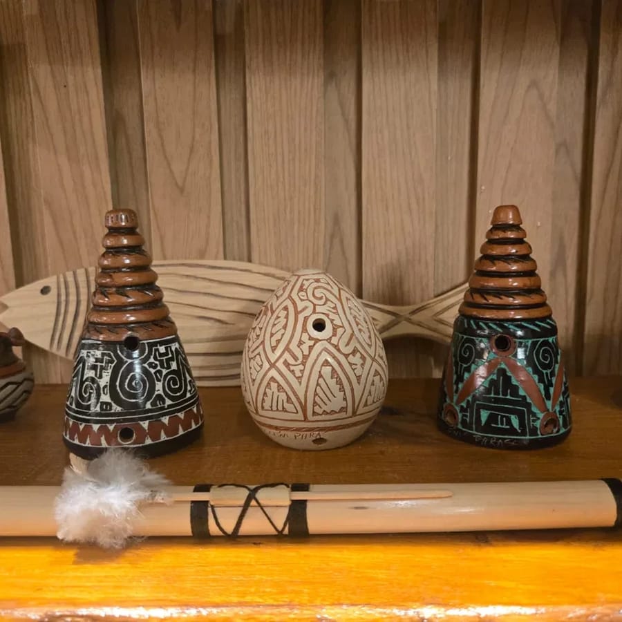 Dois cones de cerâmica com topo em degraus e grafismo marajoara, ao lado de um ovo de cerâmica clara, numa prateleira