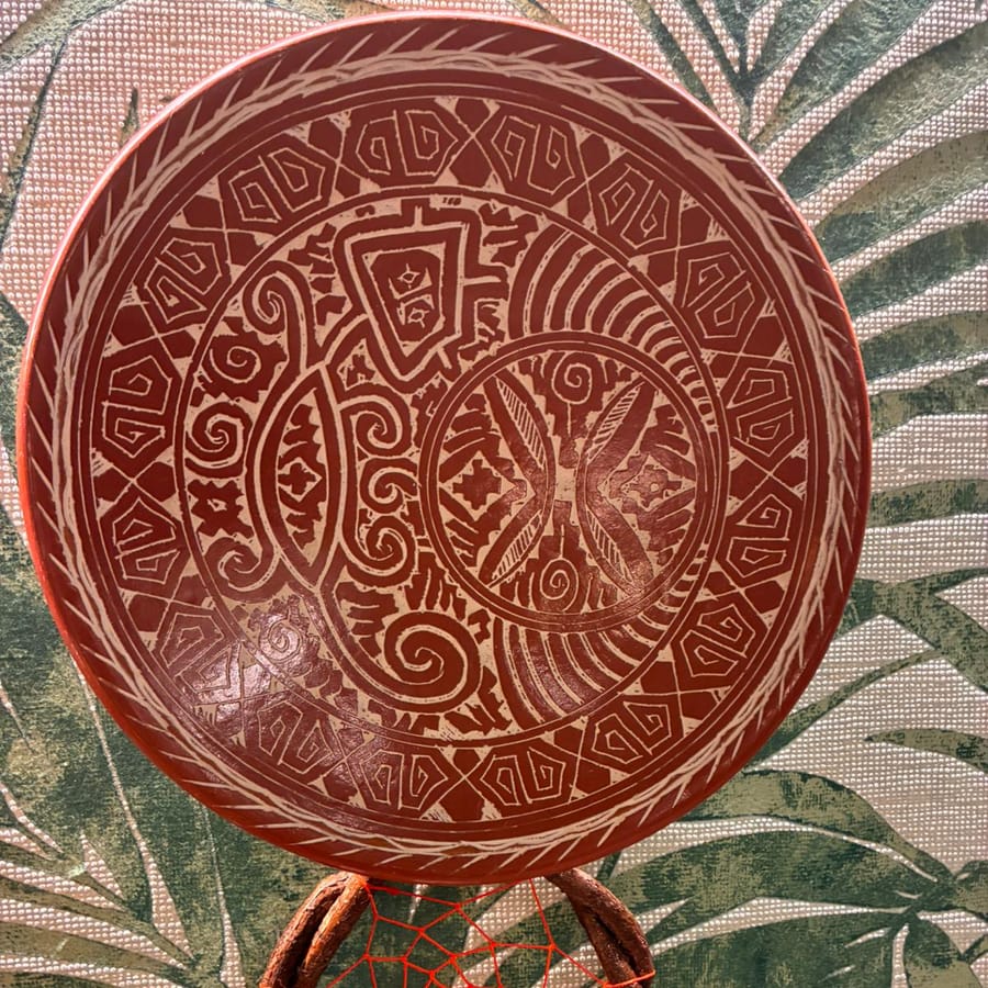 Prato de cerâmica vermelha pendurado na parede, com grafismo marajoara claro em anéis concêntricos